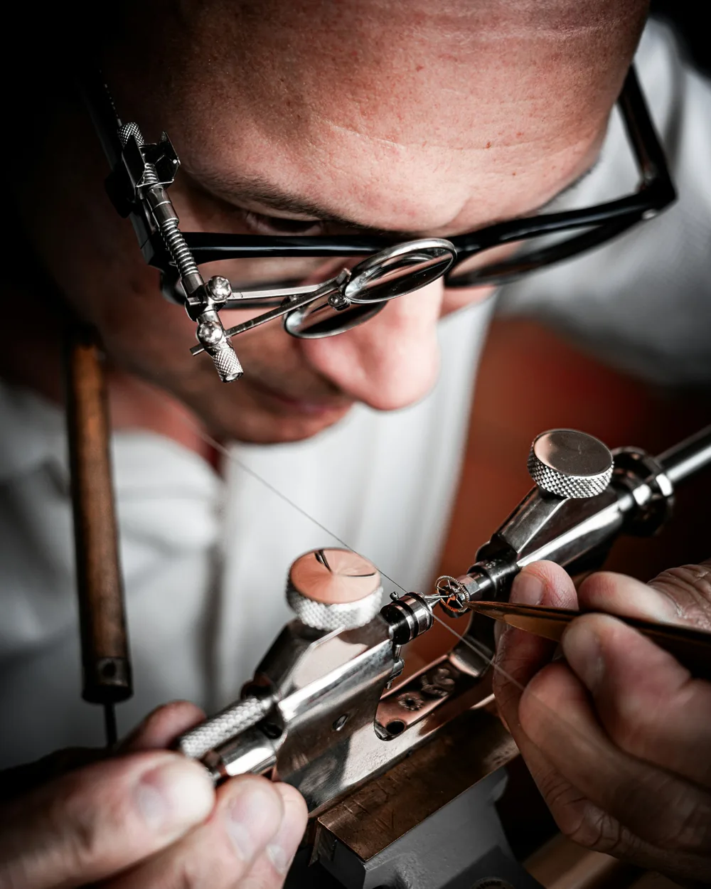Orologiaio che regola un ingranaggio con la pinzetta su un attrezzo da laboratorio